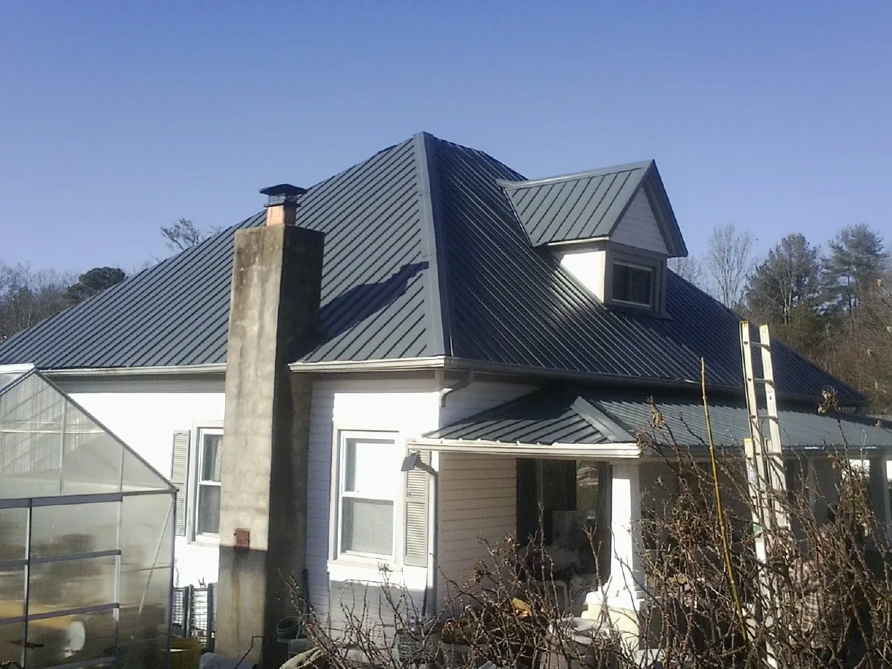 Dark blue standing seam metal roof on a white farmhouse with dormer — Slate & Tile Roof Repair by Roofing Brothers in Mountain Rest