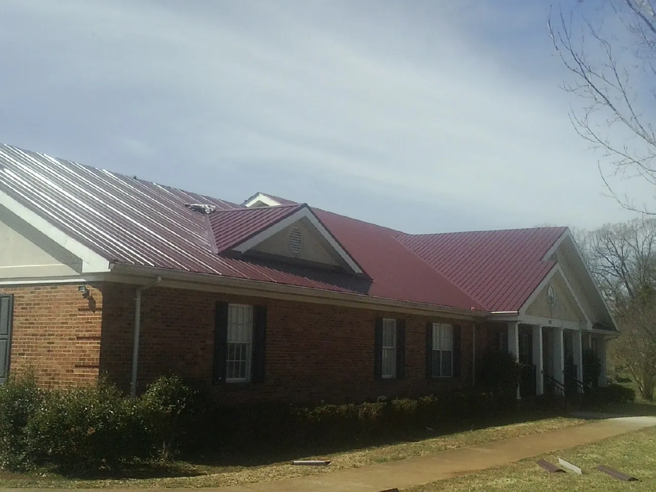 Red metal roof with gabled entries on a long brick building, from a Hail Damage Roof Repair job in Mountain Rest