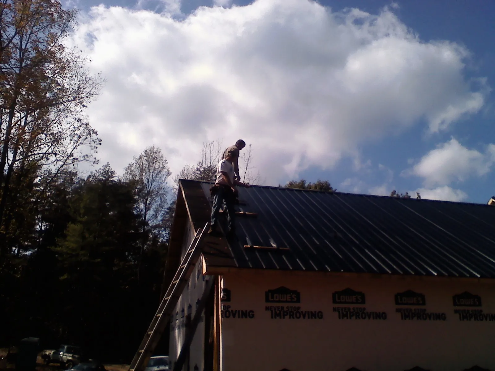 Roofer fastening dark metal panels high against a cloudy sky, from a Roof Inspection job in Mountain Rest