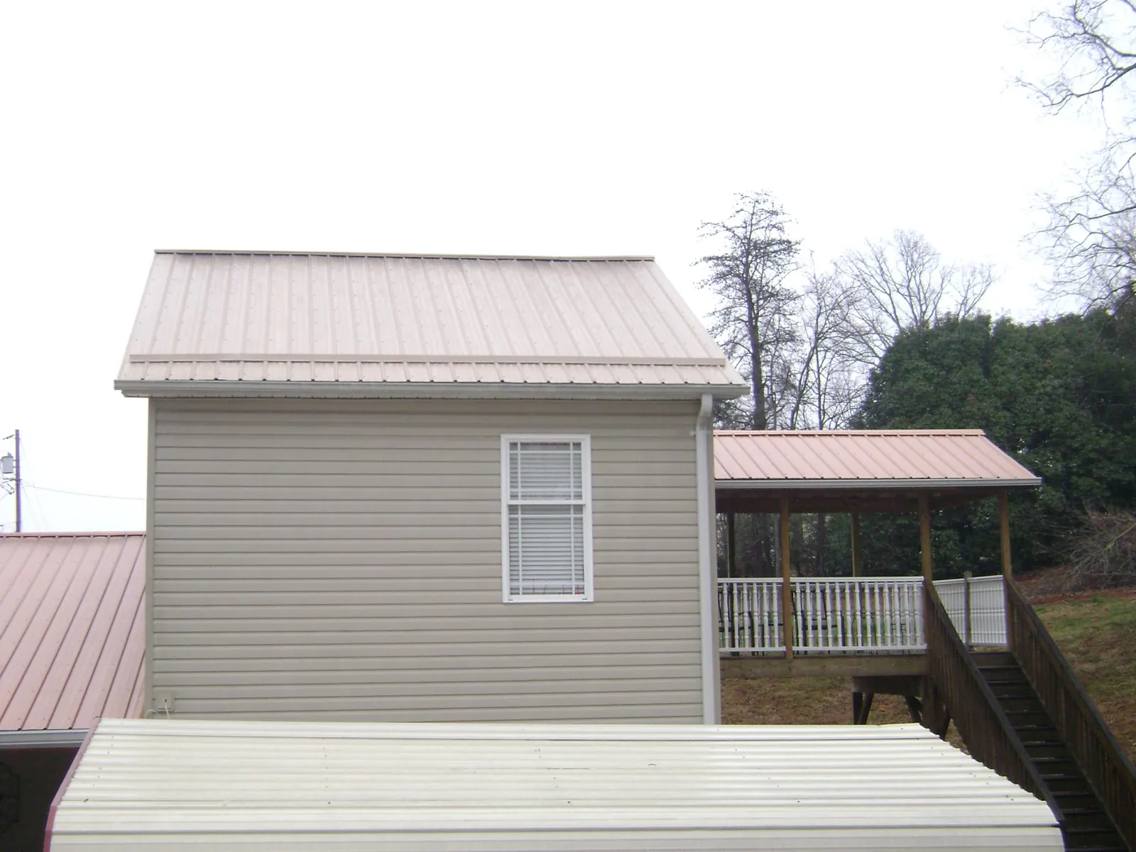Tan metal roofs on a two story addition and attached porch, from a Roof Replacement job in Mountain Rest